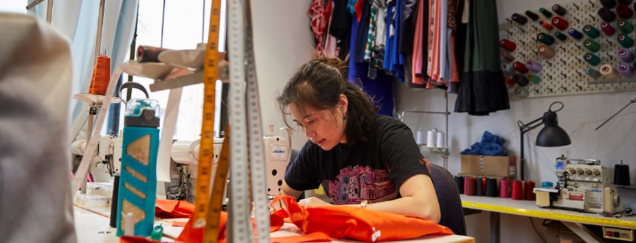 Woman busy sewing in a workshop with clothing and machinery in view