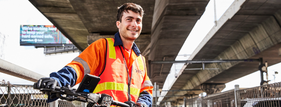Young man in orange high vis on a bike smiling to camera